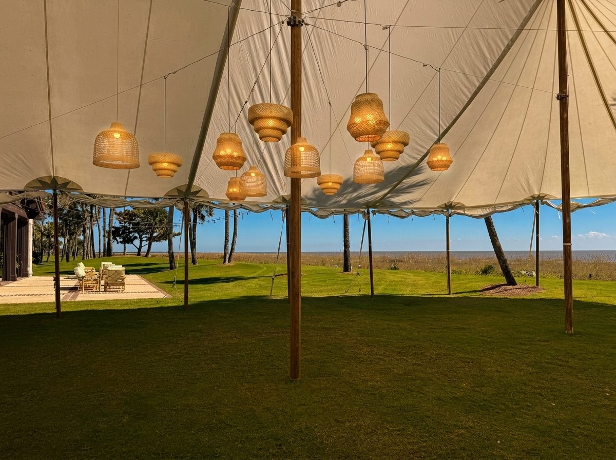 Sailcloth tent with a cluster of glowing woven-rattan lantern pendants overlooking the marsh